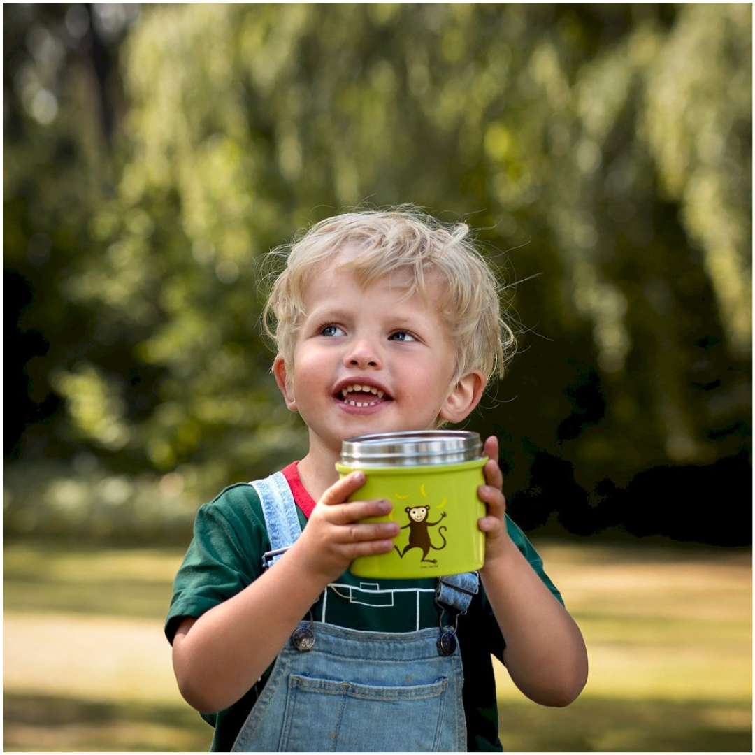Criança a sorrir segurando um recipiente verde com desenho de macaco
