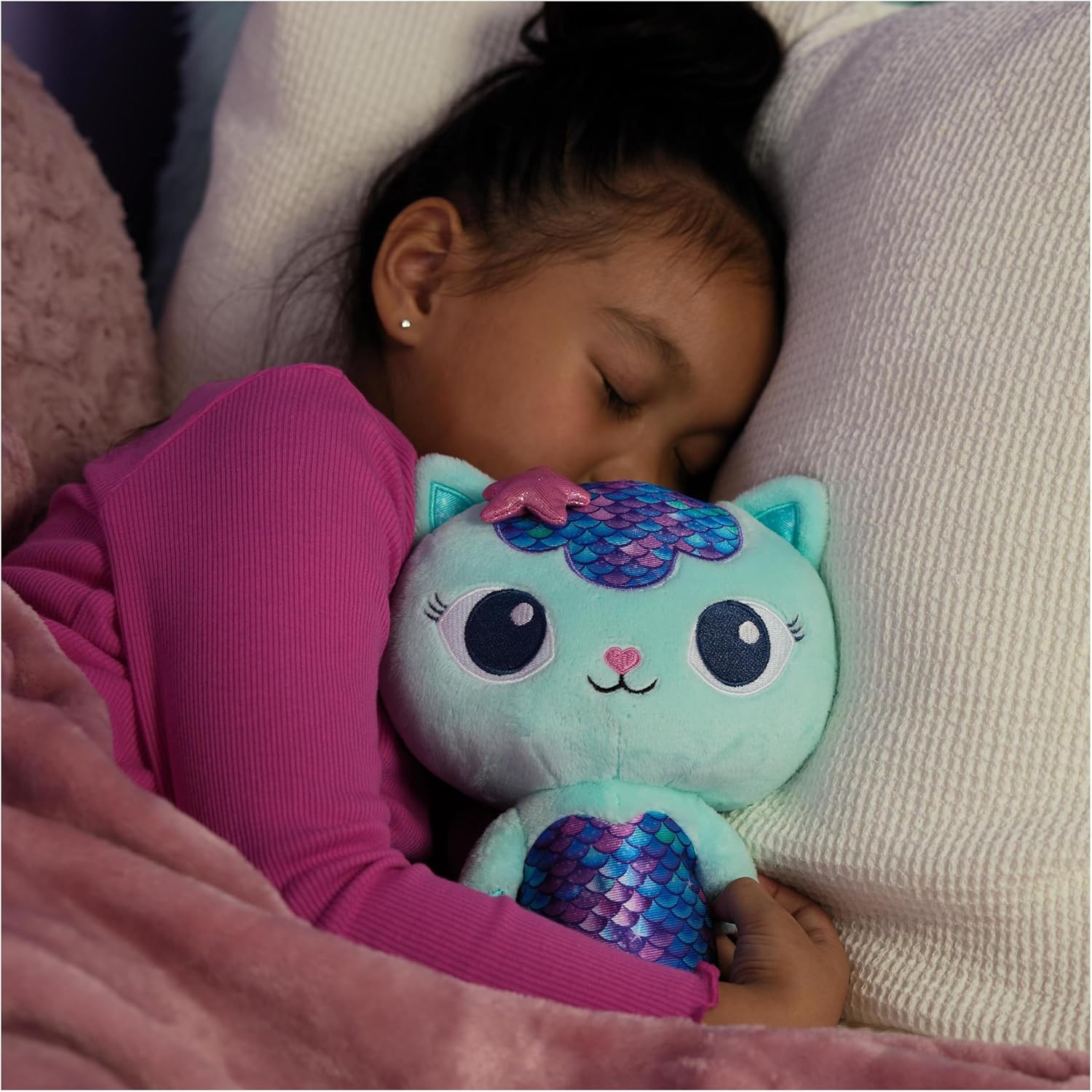 Criança a dormir com peluche de gato verde-água com escamas azuis e roxas brilhantes.