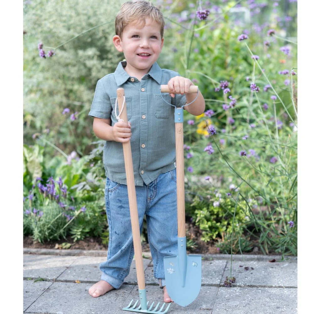 Criança com ferramentas de jardim infantis em ambiente exterior com plantas e flores.