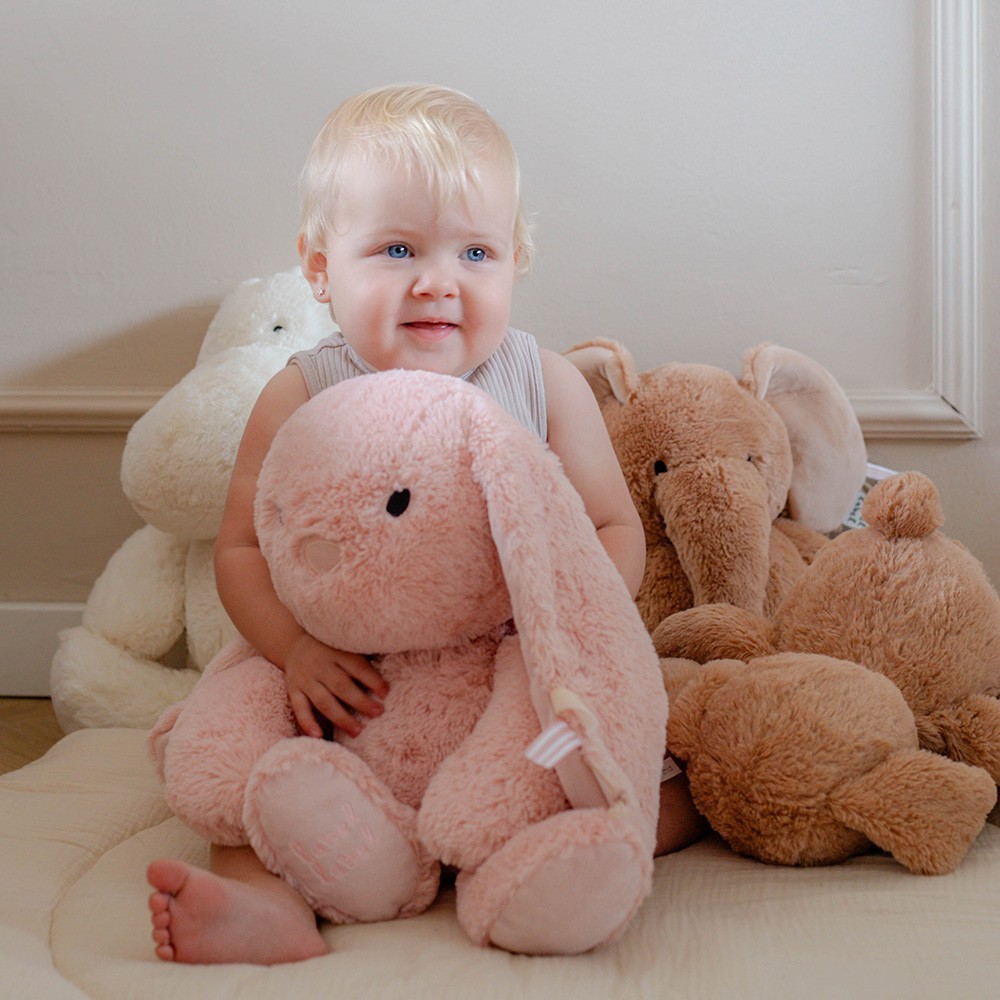 Bebé com peluches macios coloridos em tom claro sentado no chão.