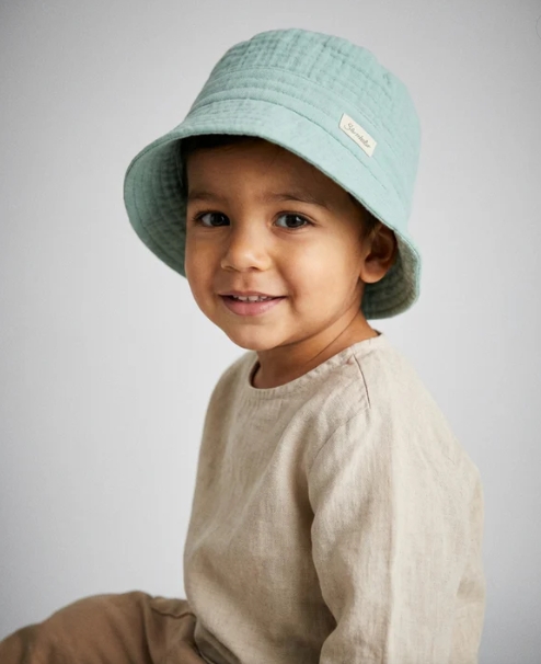 Criança com chapéu de balde azul e camisola bege em fundo branco