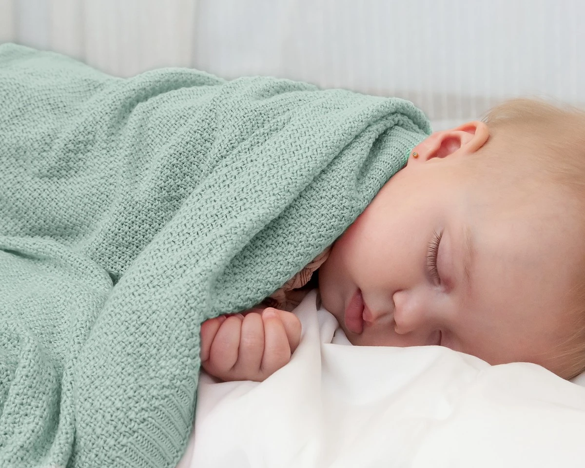 Bebé a dormir coberto com manta verde clara de malha.