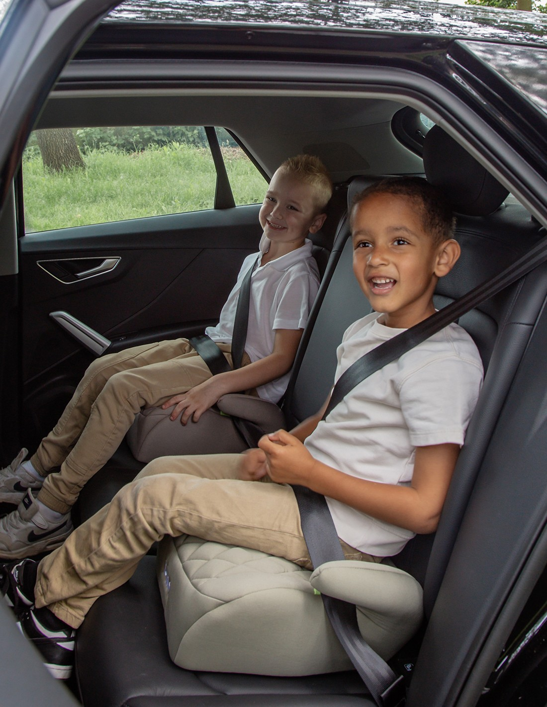 Duas crianças sentadas em assentos elevatórios dentro de um carro preto