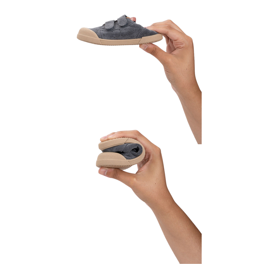Sapato infantil cinzento com sola bege e fecho velcro, em duas posições segurado por mãos.
