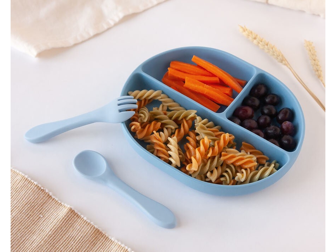 Prato infantil azul com divisórias, massa, cenoura, uvas, colher e garfo azuis