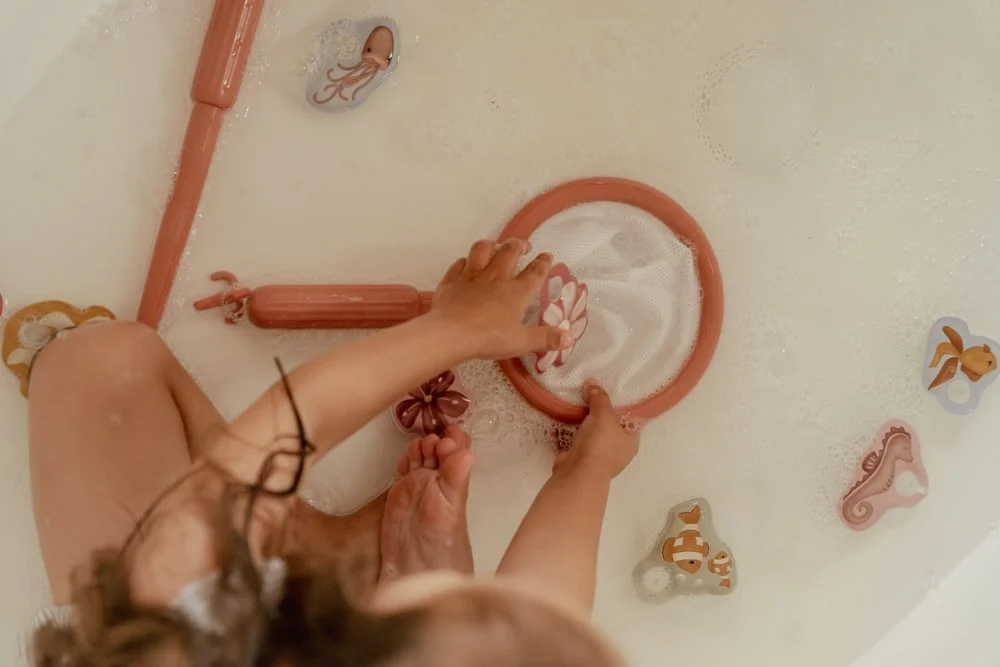 Criança a brincar com brinquedos de banho coloridos numa banheira cheia de água