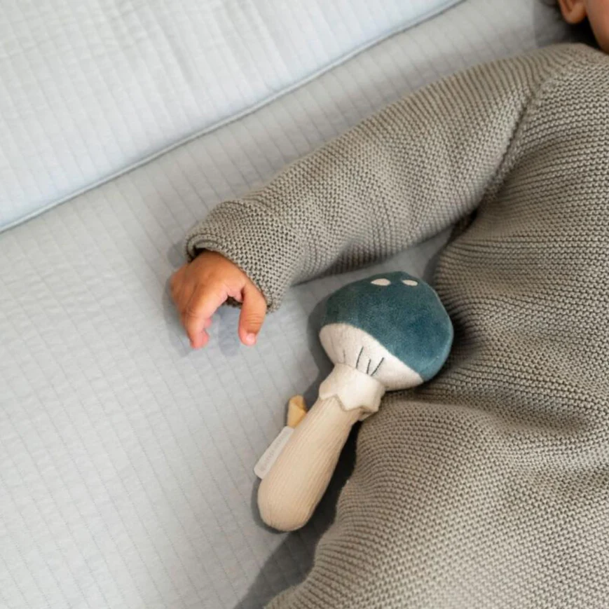 Boneco de tecido em forma de cogumelo ao lado de bebé com casaco cinza