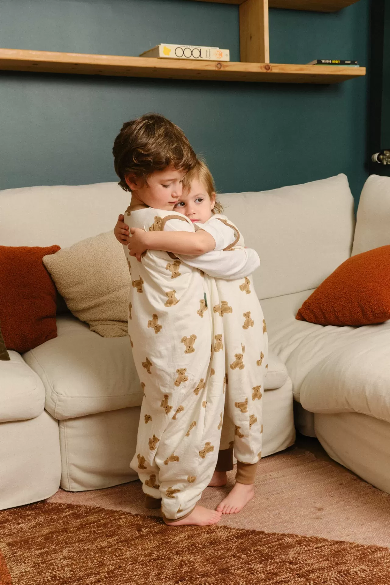 Crianças com pijamas de ursinhos abraçadas em sala com sofá branco
