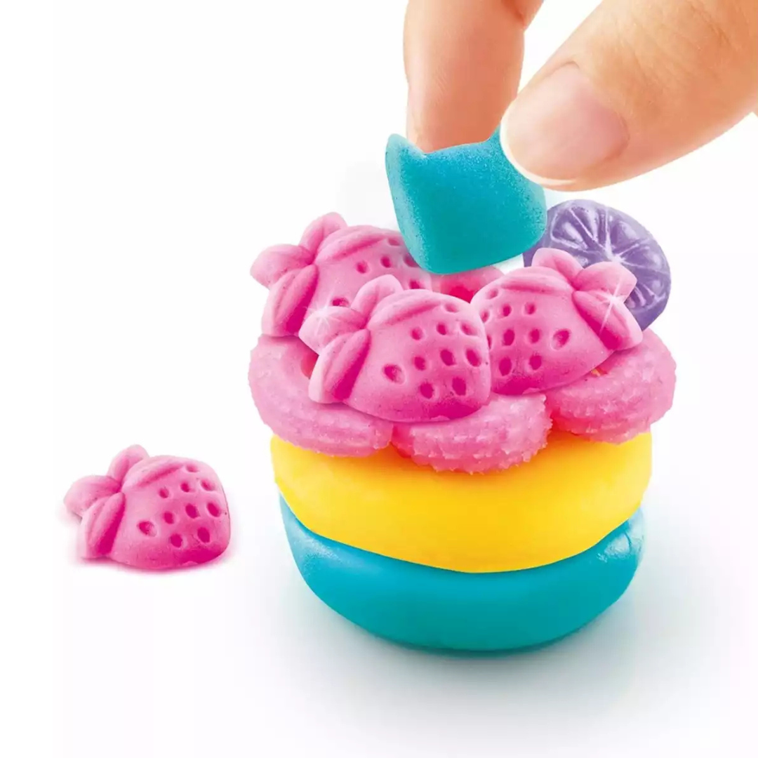 Massa moldável colorida em camadas com peças em forma de morango e mão segurando uma peça azul