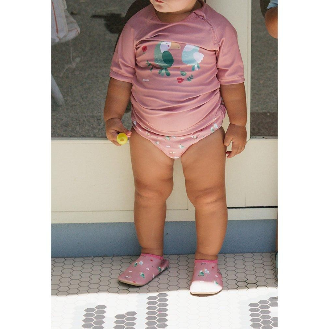 Criança com roupa de banho rosa com estampa de pássaros coloridos