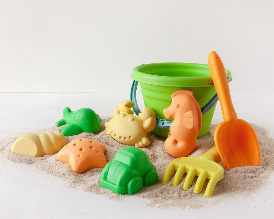 Brinquedos de praia infantis coloridos com balde verde, pá e ancinho laranja na areia