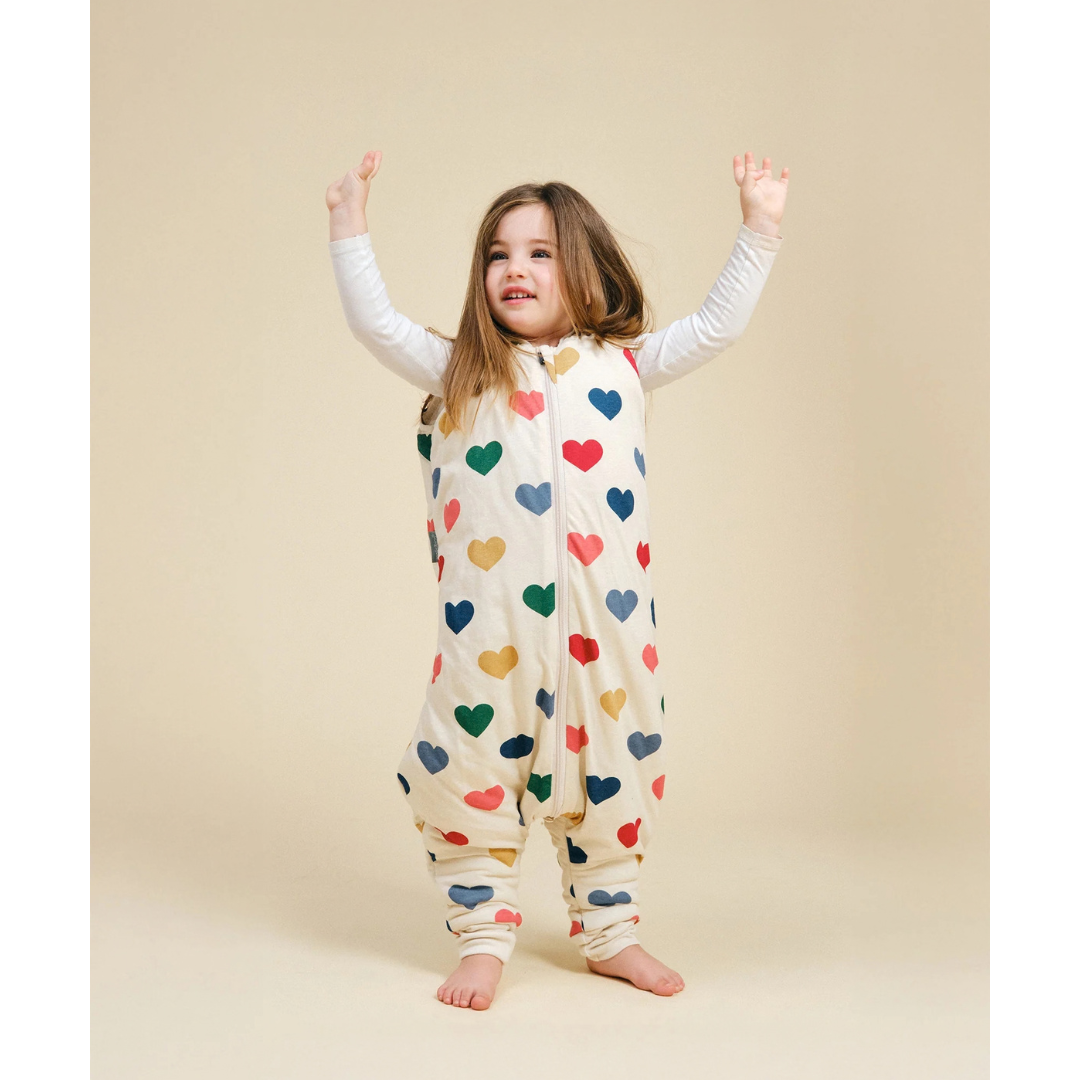 Criança com saco de dormir branco estampado com corações coloridos
