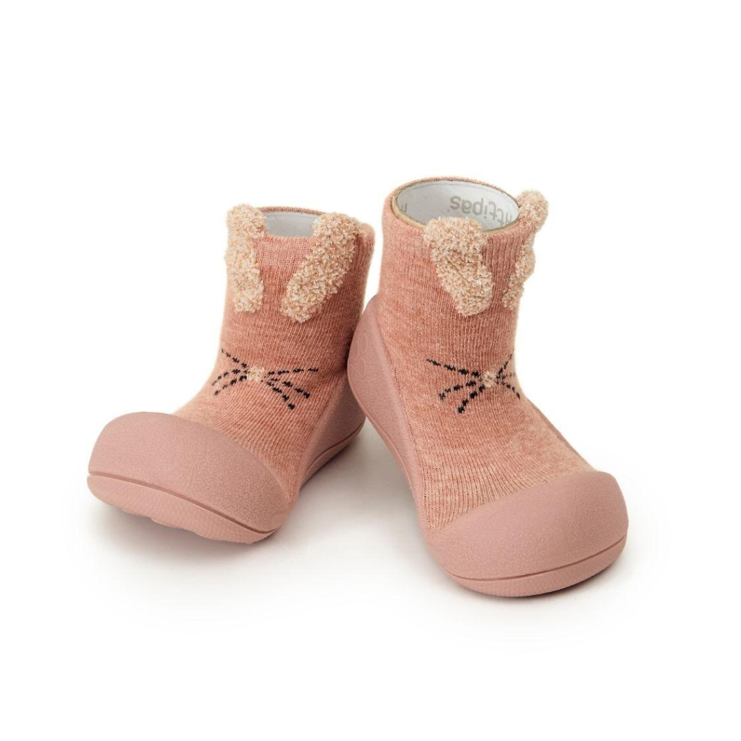 Sapatos de criança rosa com orelhas e rosto de coelho em fundo branco.