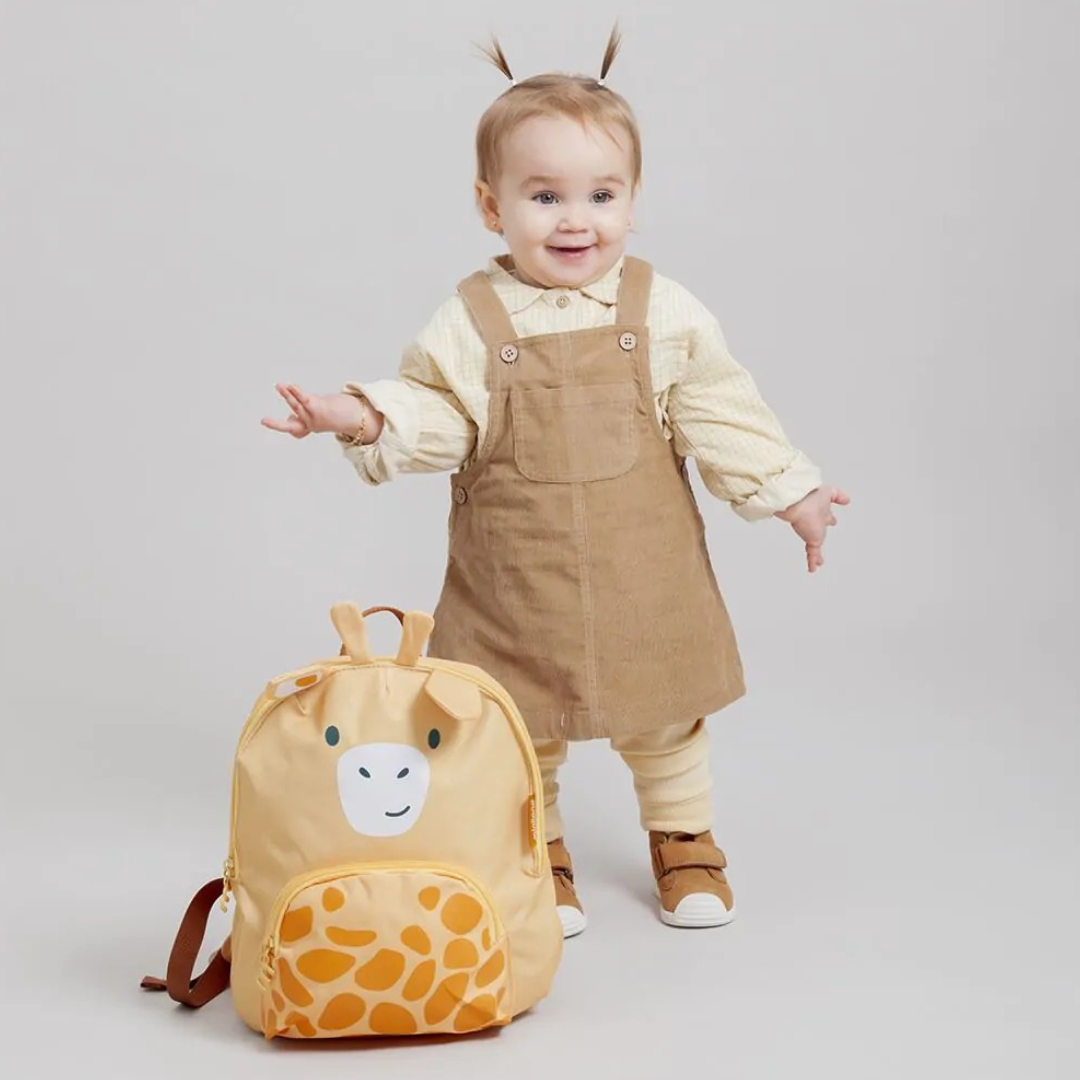 Criança com vestido castanho e mochila amarela com estampa de girafa