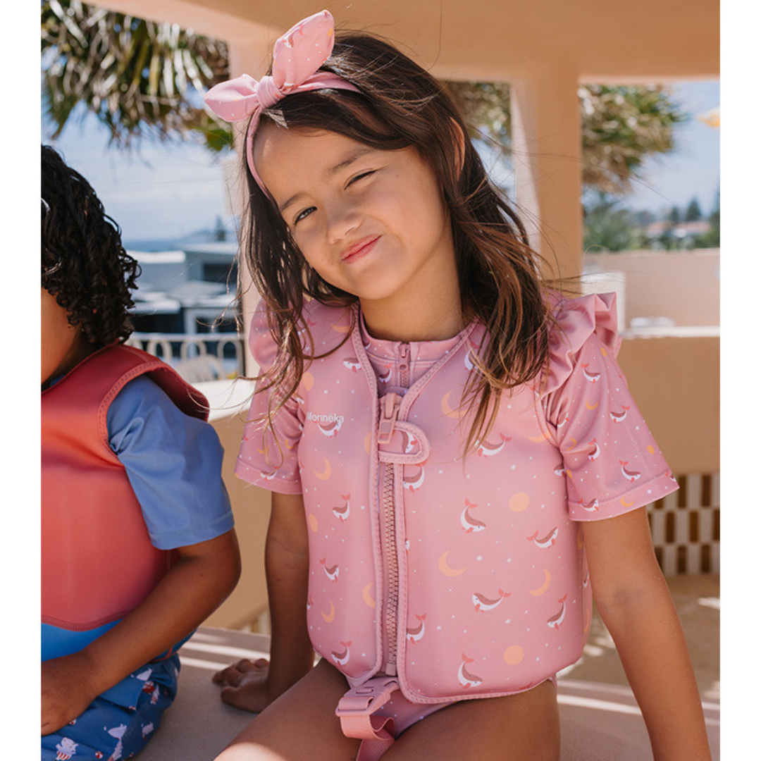 Criança com colete salva-vidas rosa estampado e faixa de cabelo cor-de-rosa