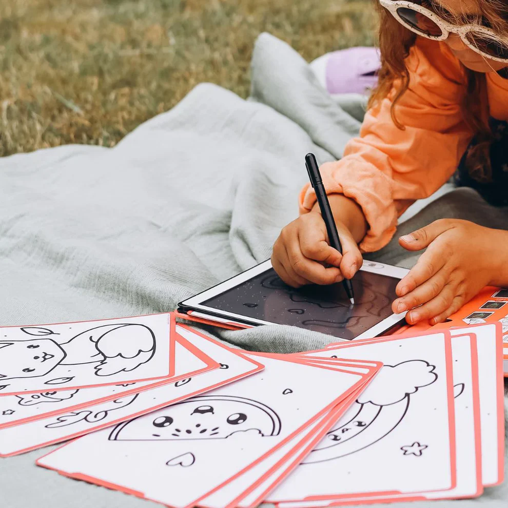 Tablet branco com caneta e cartões de desenhos infantis numa manta cinza