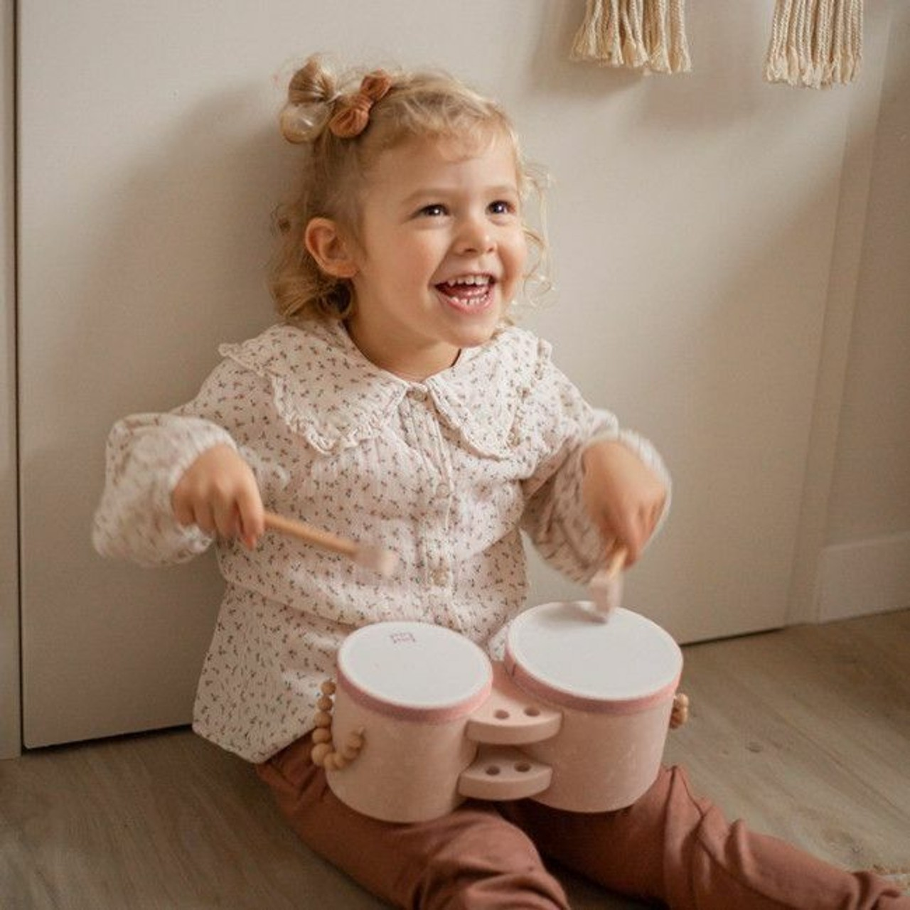 Criança a tocar tambores infantis cor-de-rosa sentada no chão