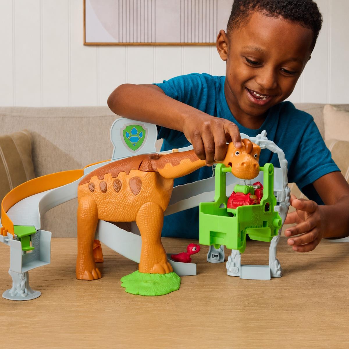 Menino a brincar com brinquedo de dinossauro laranja com escorregas numa sala.