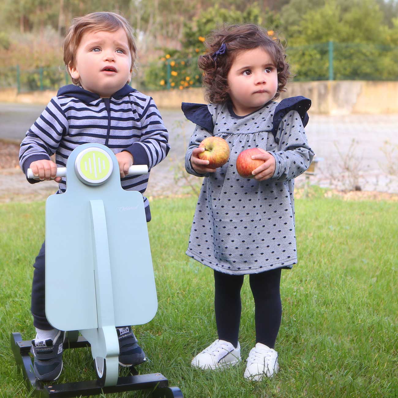 Duas crianças pequenas em parque com brinquedo e maçãs