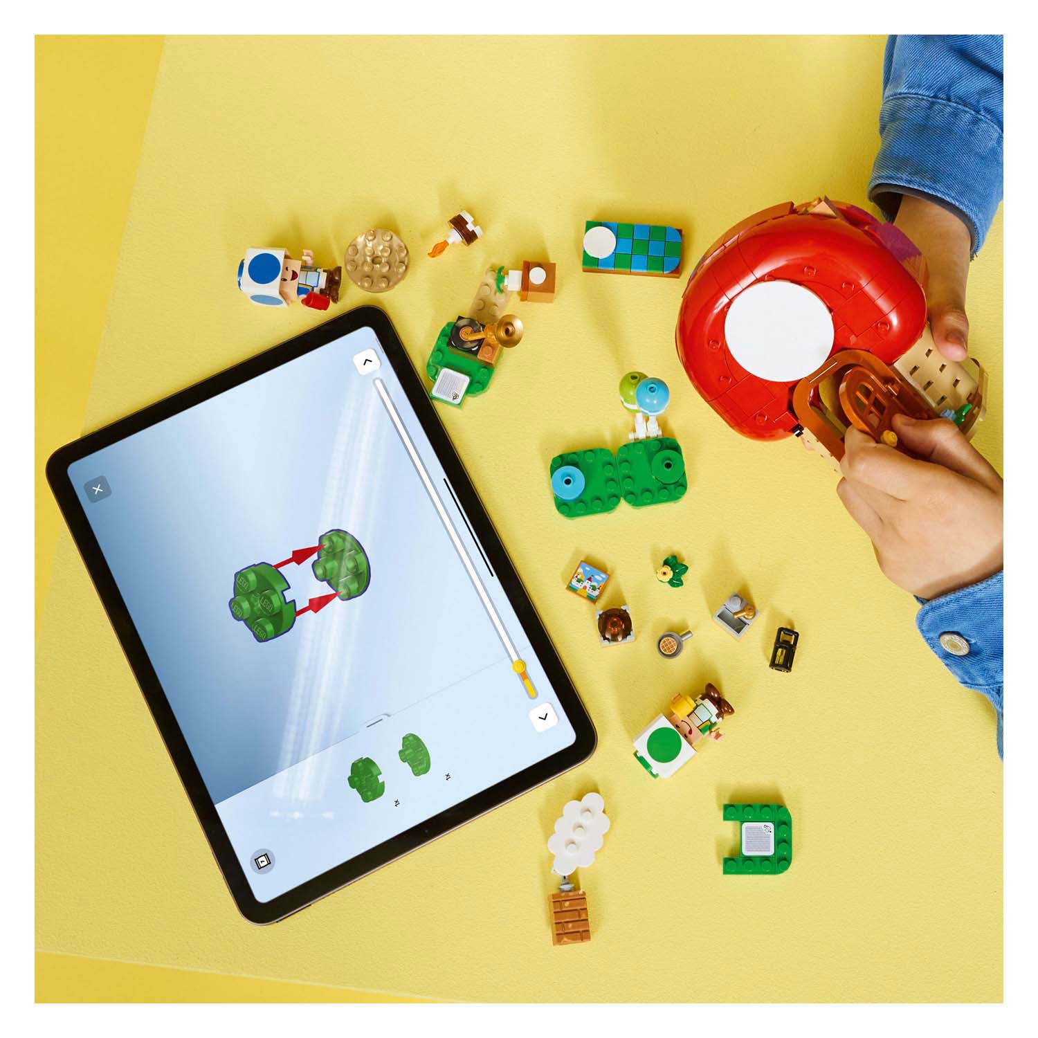 Peças de Lego coloridas e um tablet com instruções digitais numa superfície amarela