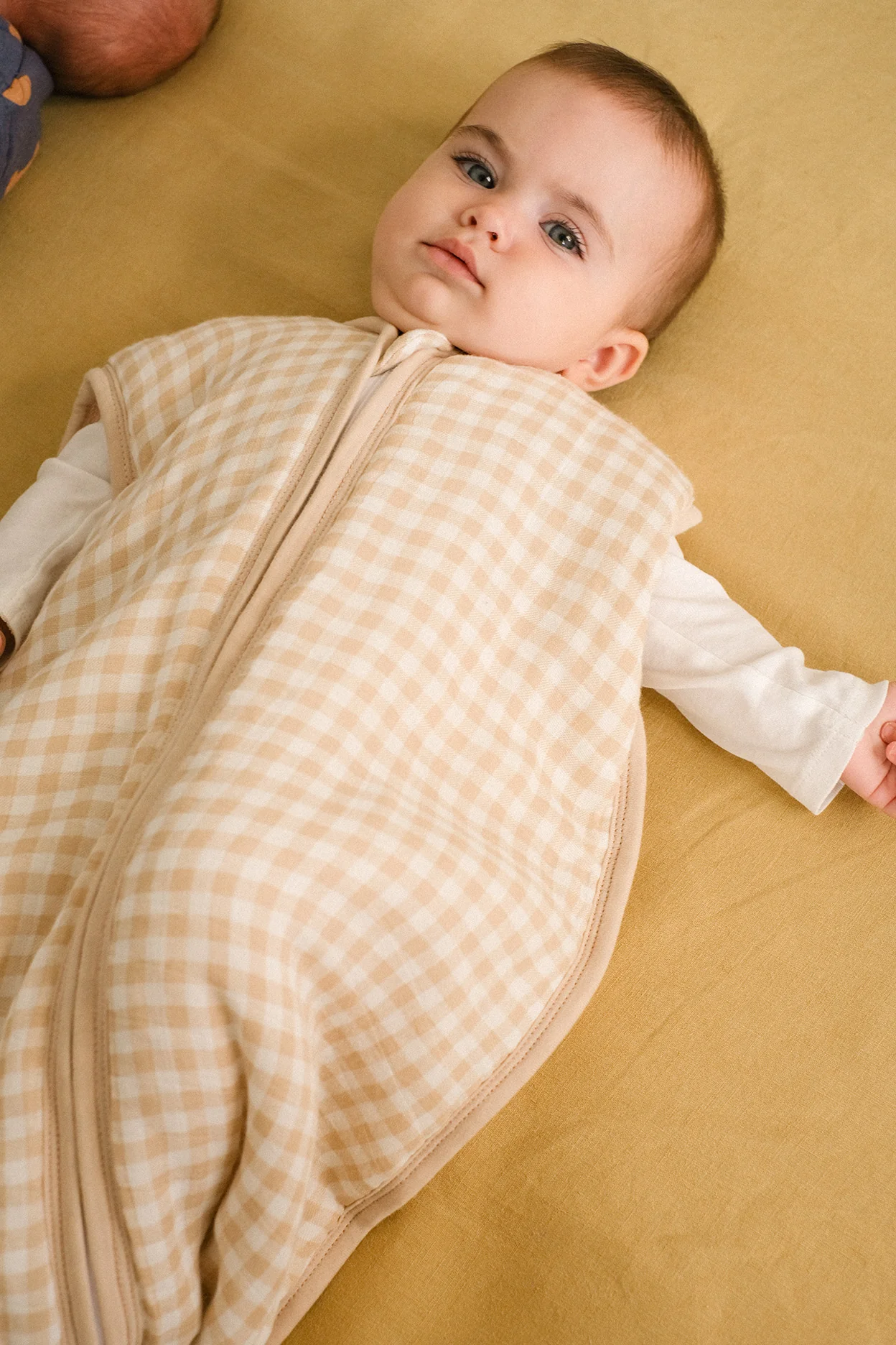 Bebé deitado com saco de dormir xadrez bege e branco
