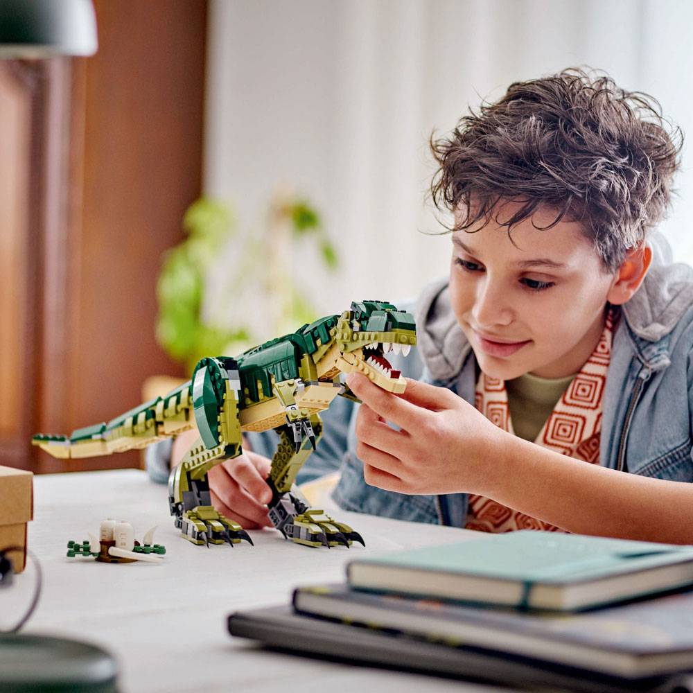 Criança a brincar com boneco dinossauro T-Rex de blocos de montar sobre mesa com livros e objetos