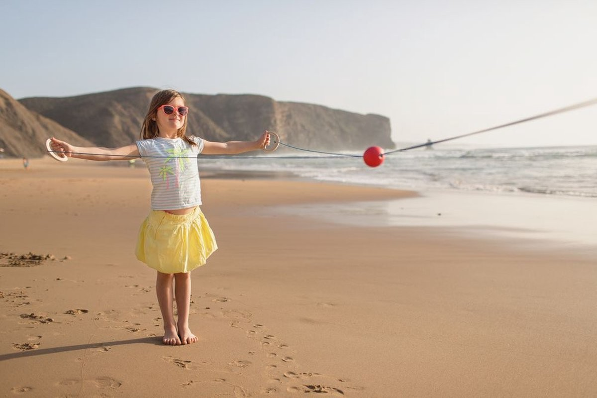 Criança a brincar na praia com bola vermelha presa a corda elástica