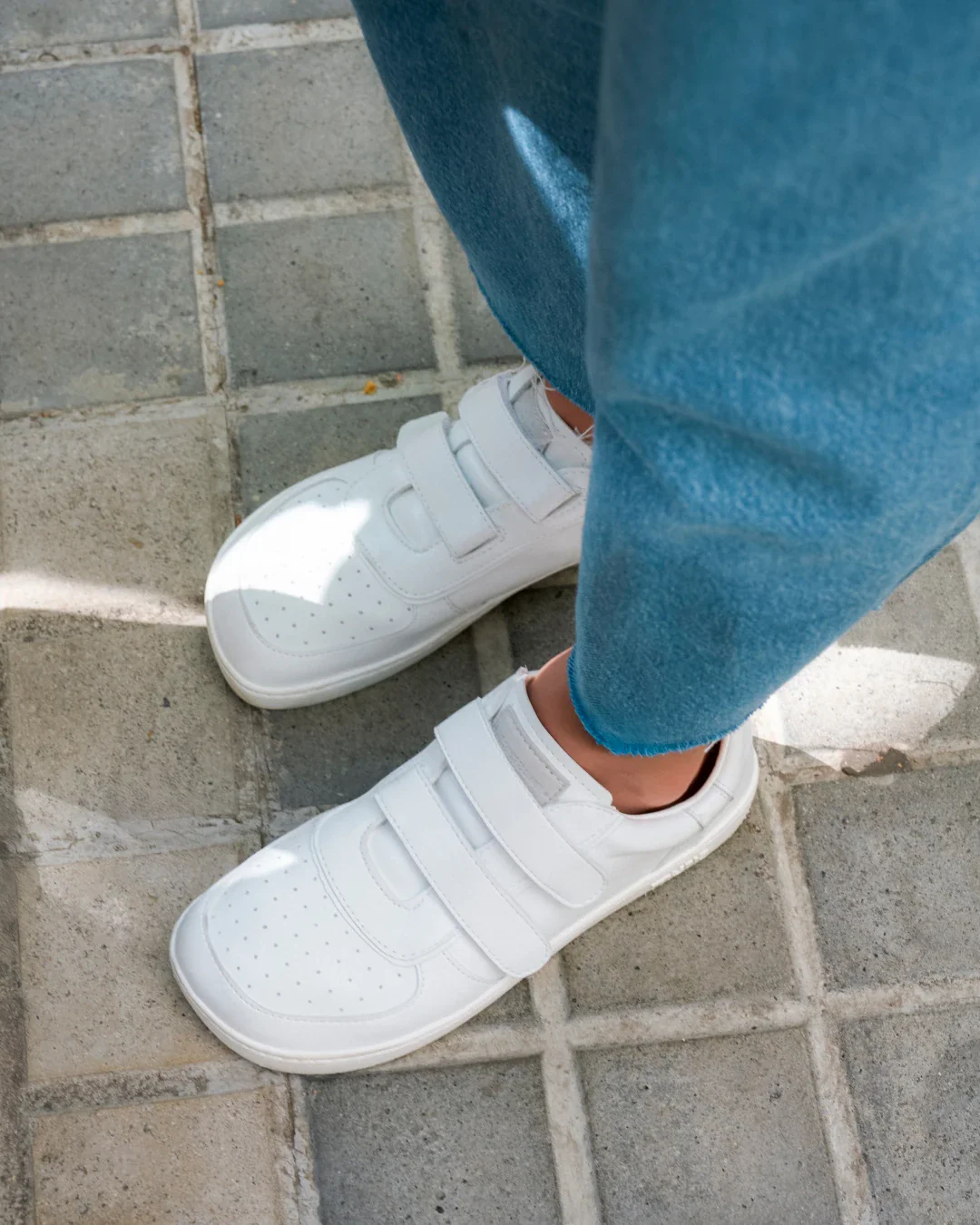 Sapatos brancos de couro com fecho de velcro e calças de ganga