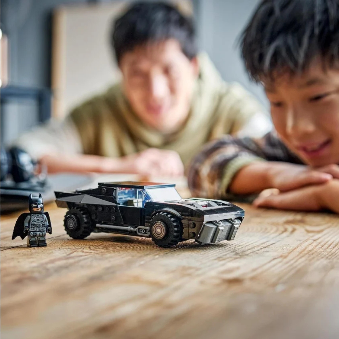 Brinquedo de construÃ§Ã£o de carro preto e figura do Batman em miniatura sobre mesa de madeira