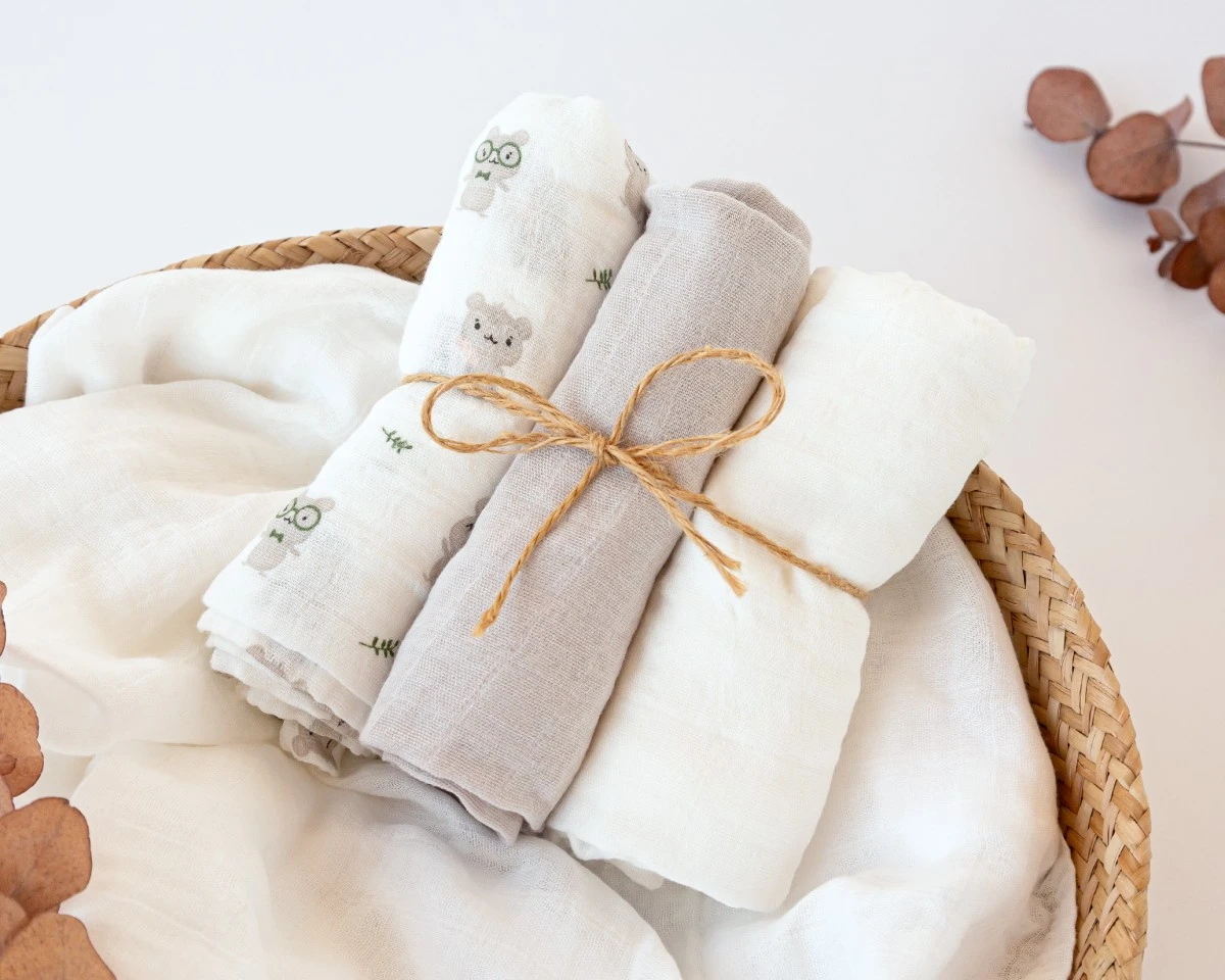 Três panos de musselina enrolados com padrões e cores neutras num cesto de palha