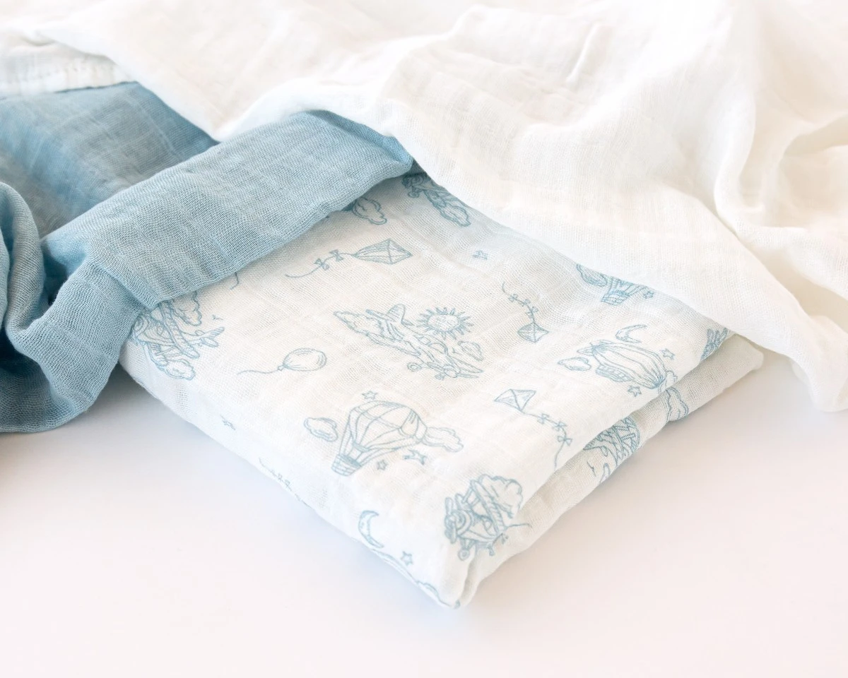 Manta branca com padrão azul de balões e pipas, com tecidos branco e azul claro