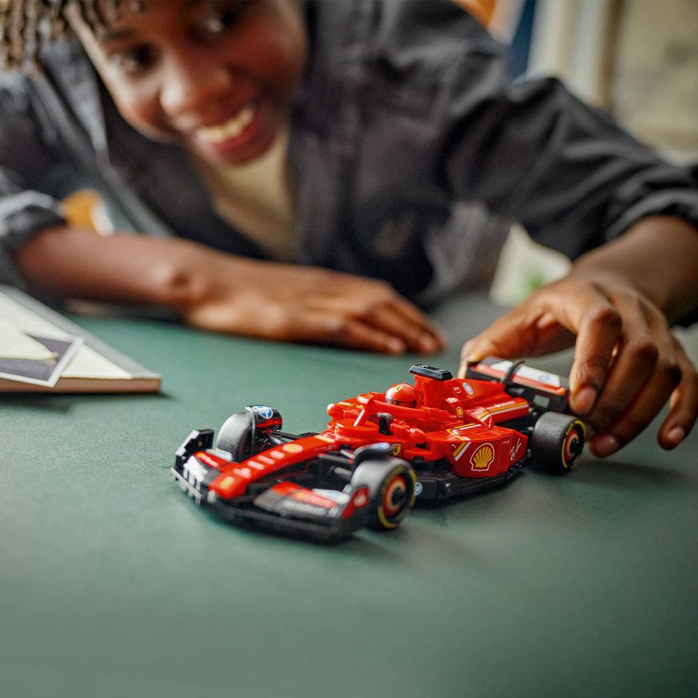 Carrinho de corrida Fórmula 1 vermelho em miniatura numa mesa verde com mãos de criança a mexer no carro.