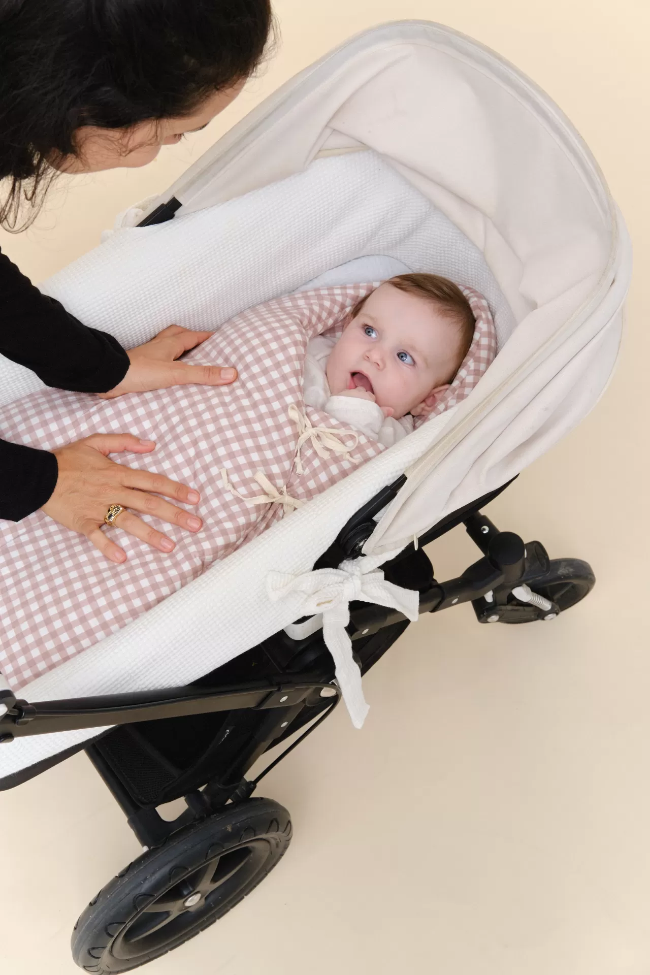 Bebé confortável num carrinho branco com saco de dormir xadrez rosa e branco.
