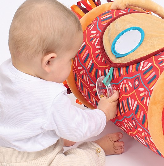 Bebé a brincar com brinquedo macio colorido vermelho e laranja com padrões geométricos.