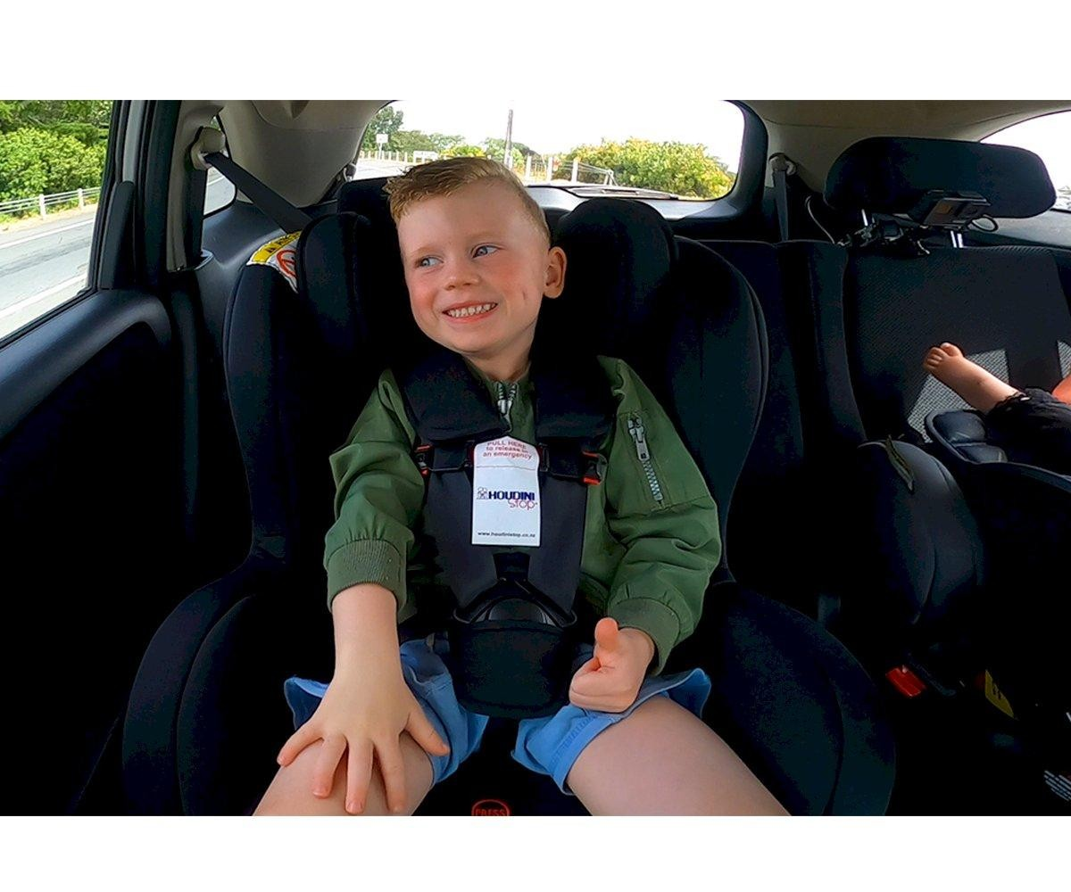 Criança em cadeirinha auto preta num carro com cinto de segurança e etiqueta branca