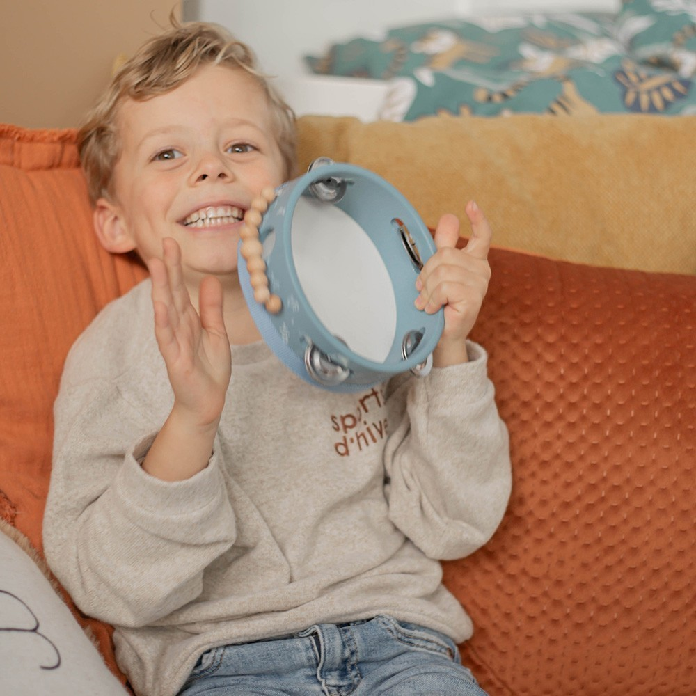 Criança a tocar pandeiro azul sentada em sofá com almofadas coloridas