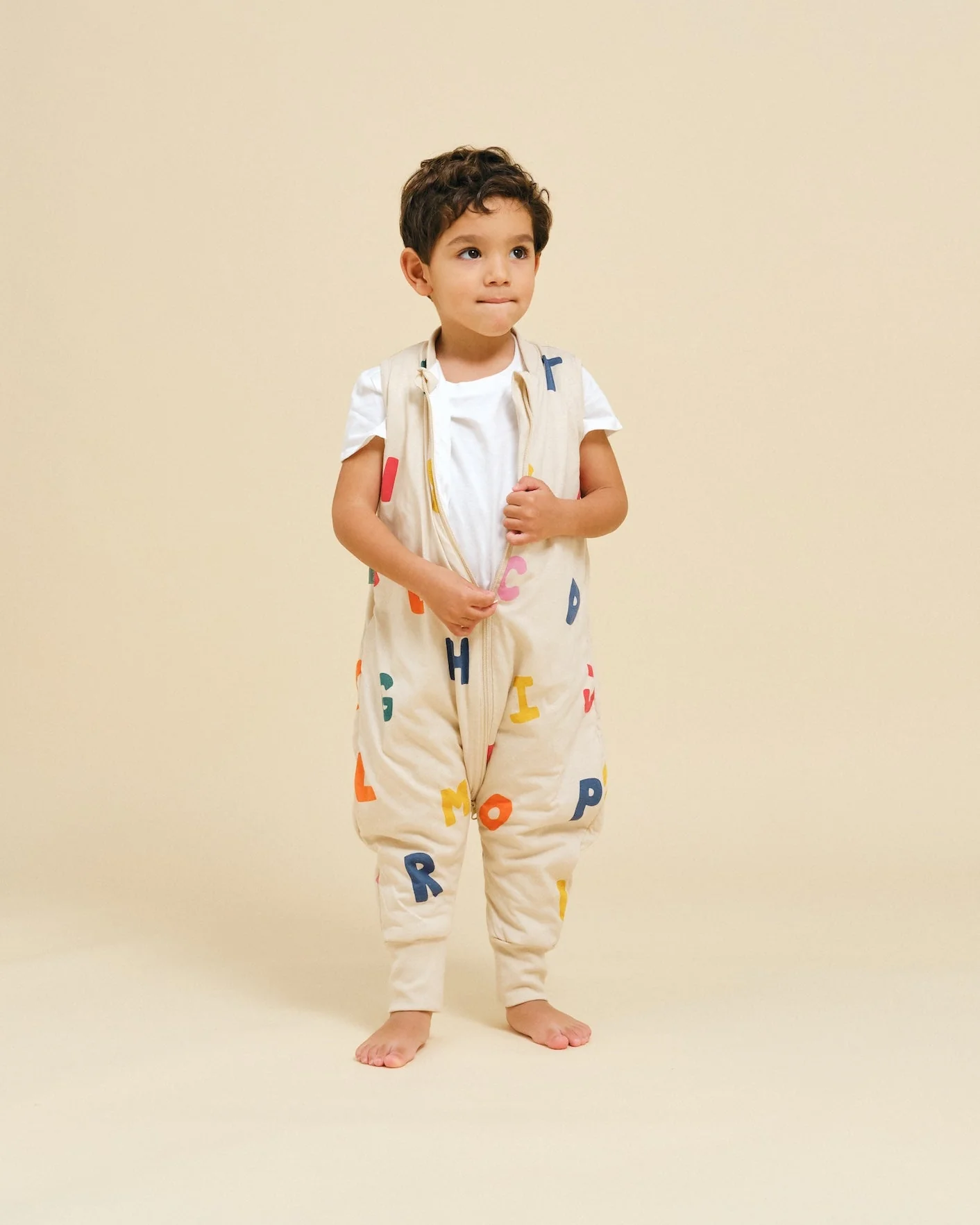 Criança com pijama acolchoado bege com letras coloridas em fundo bege neutro