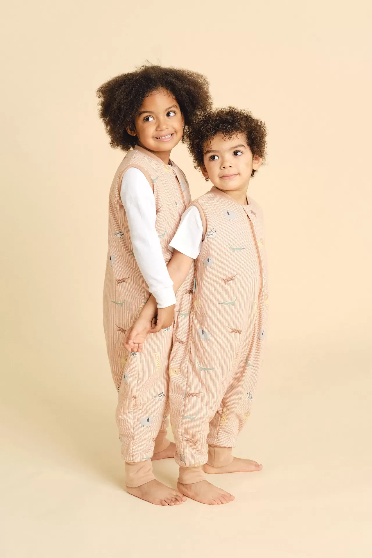 Duas crianças com macacões cor-de-rosa claro com padrão de animais