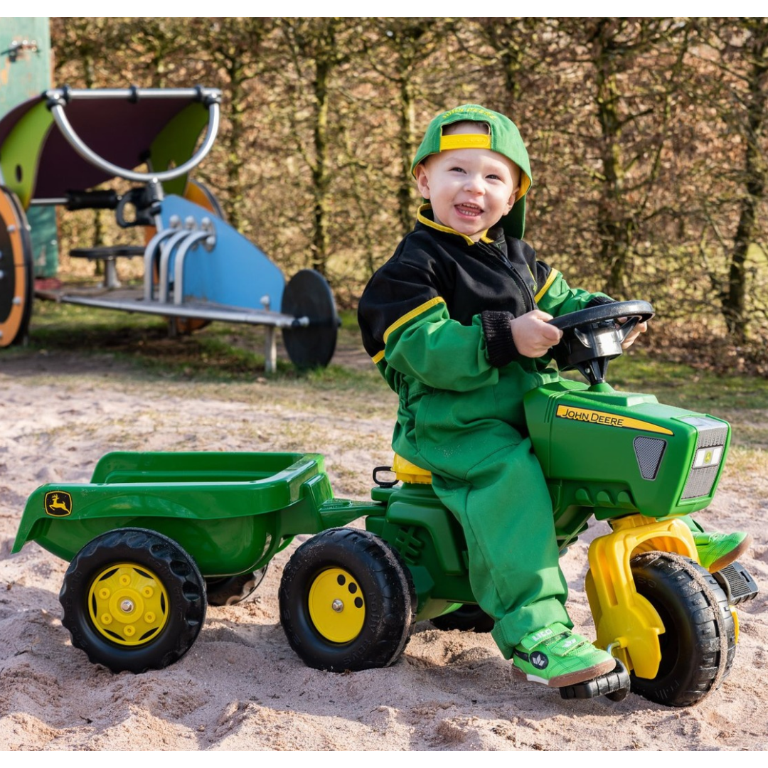 Criança num tractor John Deere verde e amarelo de brincar ao ar livre na areia.