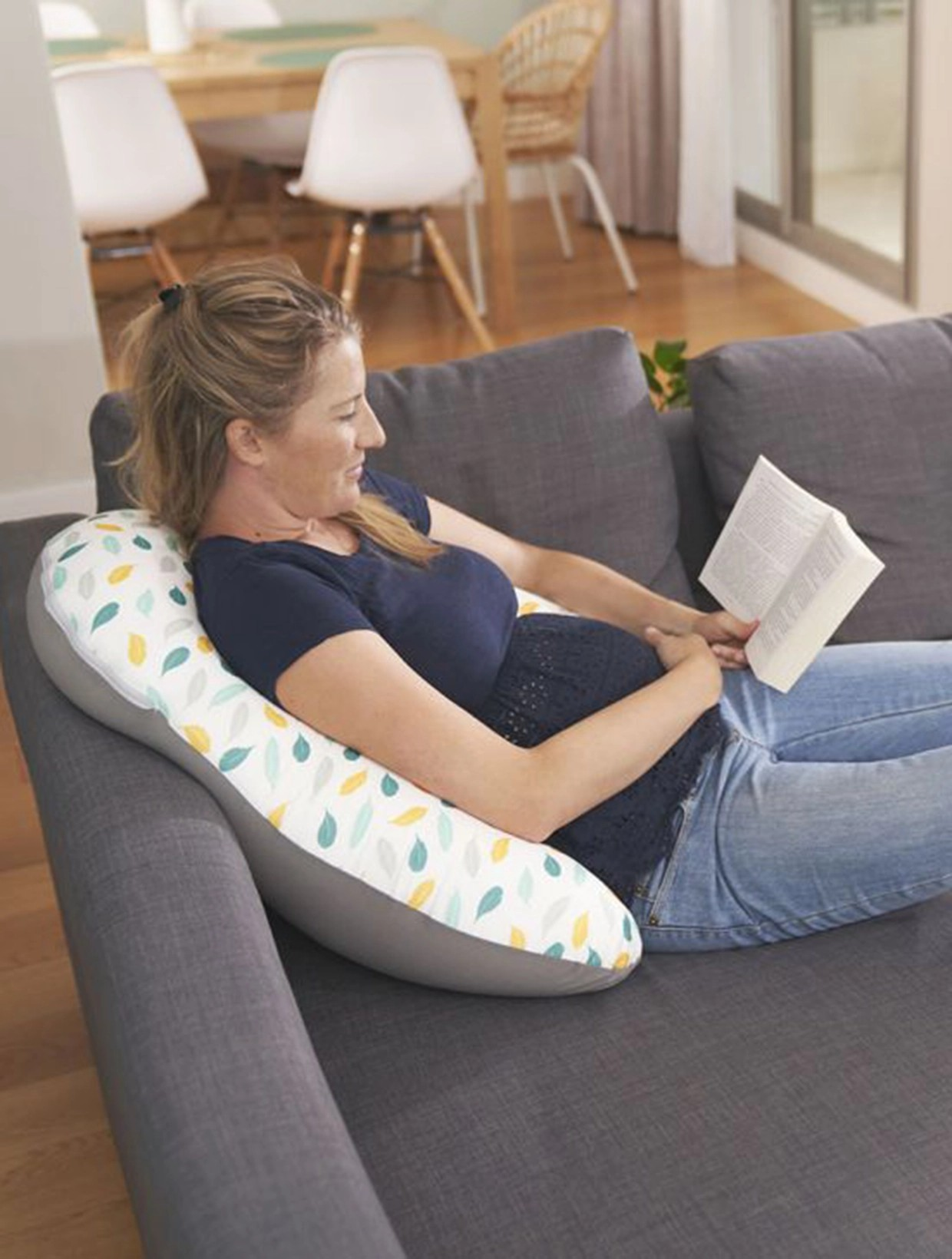 Mulher sentada no sofá a usar almofada comprida de padrão folhas coloridas