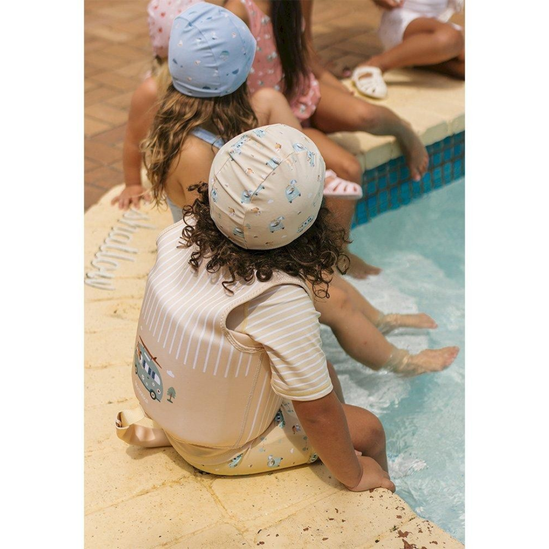 Criança com touca e fato de banho sentado à beira da piscina