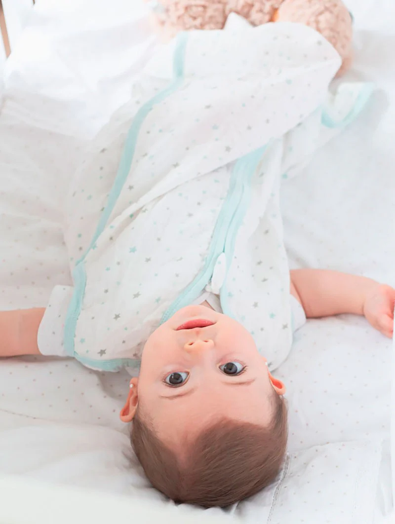 Bebé deitado de costas com saco de dormir branco com estrelas cinzentas e azul claro.