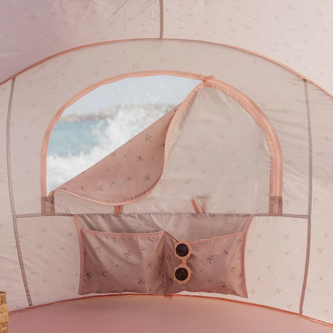 Interior de tenda rosa claro com padrão floral, janela com cortina enrolada e bolsos com óculos de sol