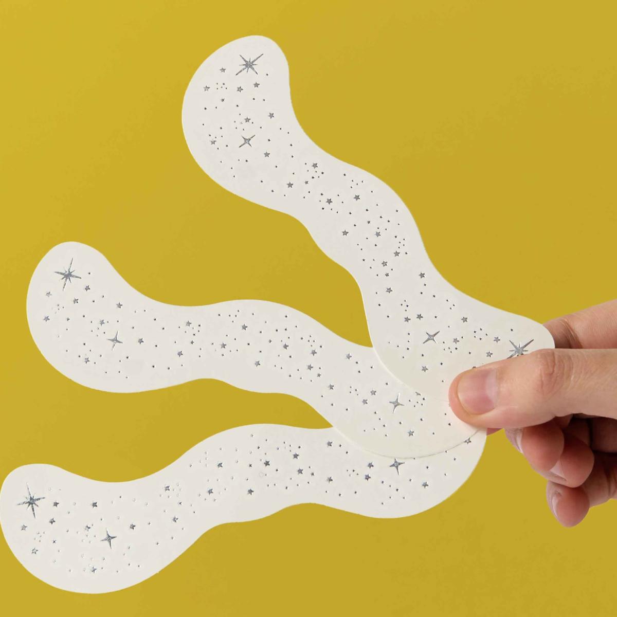 Adesivos brancos com padrão de estrelas cinzentas e pretas seguidos por uma mão em fundo amarelo