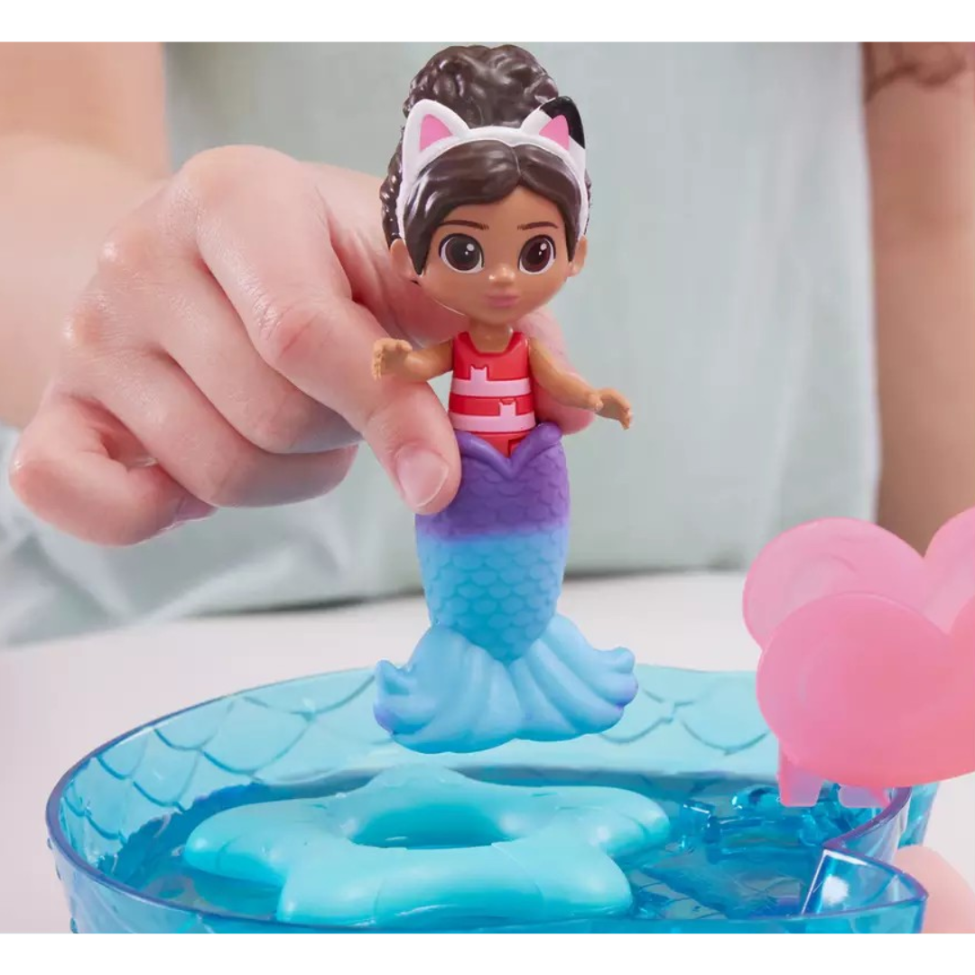 Boneca sereia colorida segurada à mão sobre brinquedo de água azul e rosa
