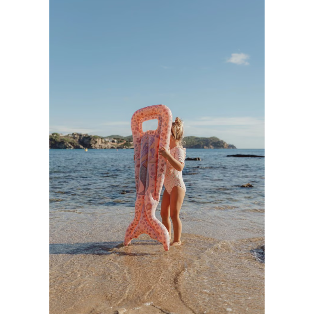Criança na praia com colchão insuflável cor-de-rosa com desenhos marinhos