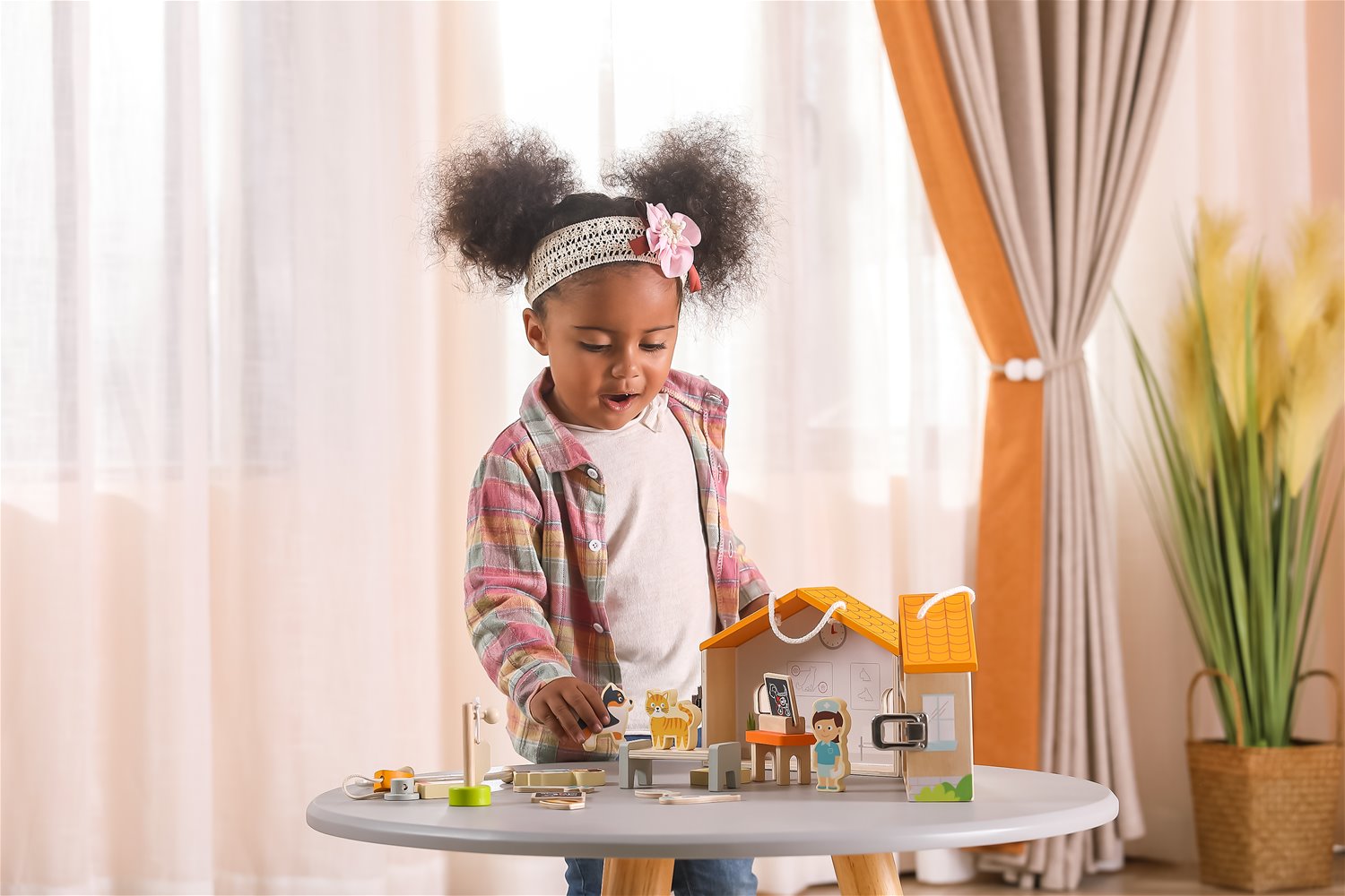 Criança a brincar com casinha de brinquedo de madeira numa mesa redonda cinzenta.