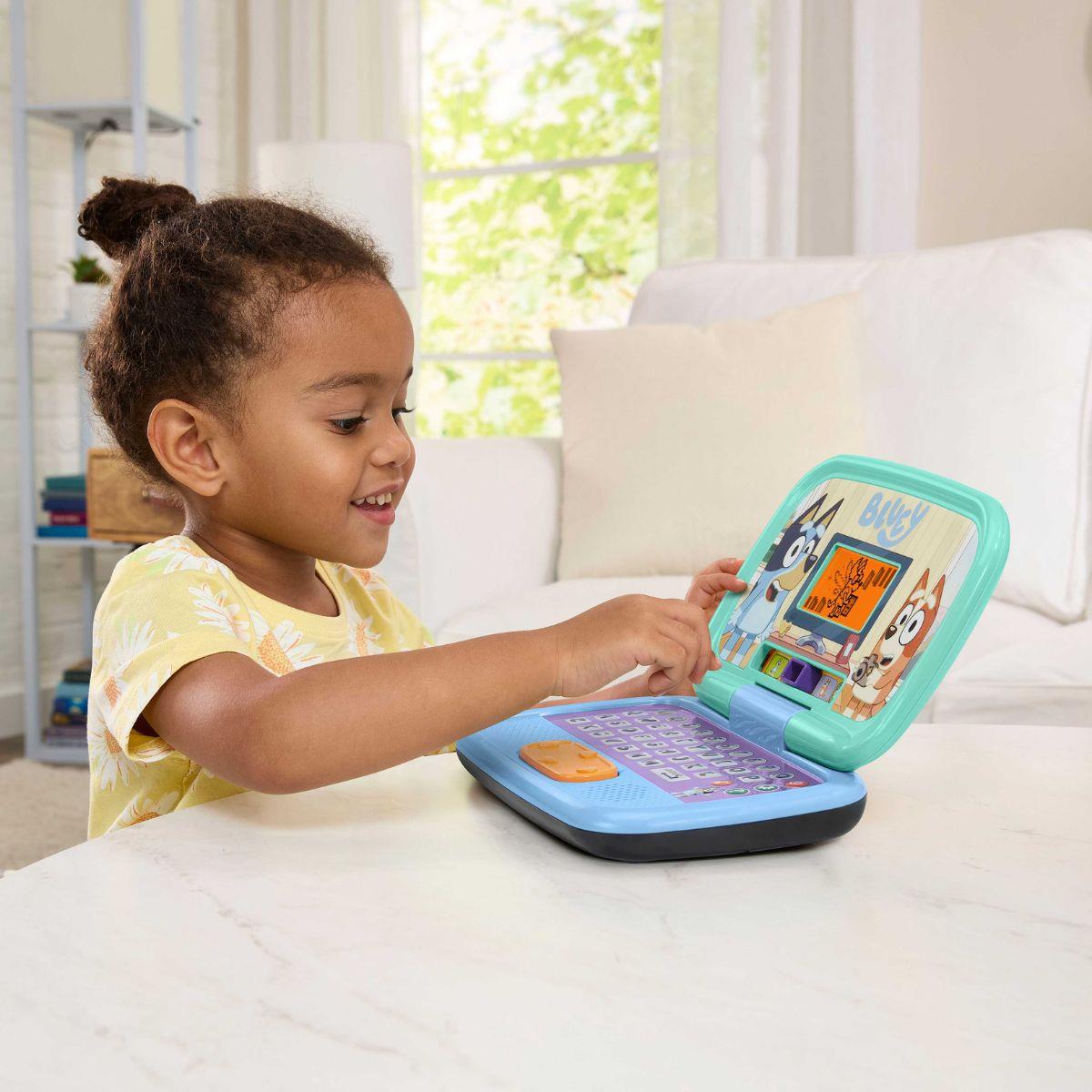 Menina a brincar com computador de brinquedo colorido com desenhos animados