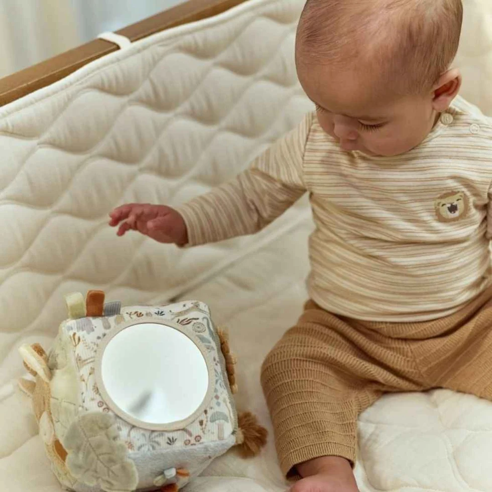 Bebé sentado em berço acolchoado com brinquedo macio e espelho