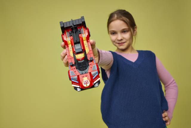 Criança com carro de brinquedo vermelho e número 51 em fundo amarelo